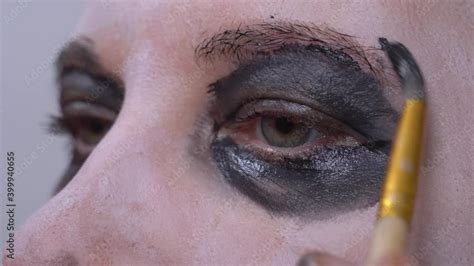 Professional makeup artist applies unusual black makeup to eyes of actress for shooting horror ...