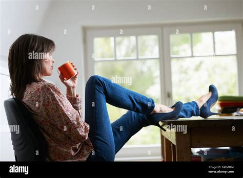 Mature Woman With Feet On Desk Drinking Coffee Stock Photo Alamy