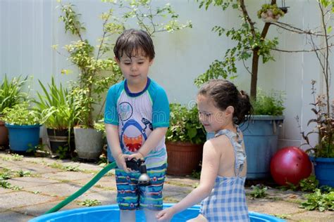 Brother And Sister Playing With Water In The Backyard On A Hot Summer