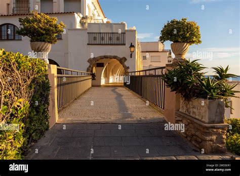 Footbridge With Potted Plants Leading To Archway Of White Hotel