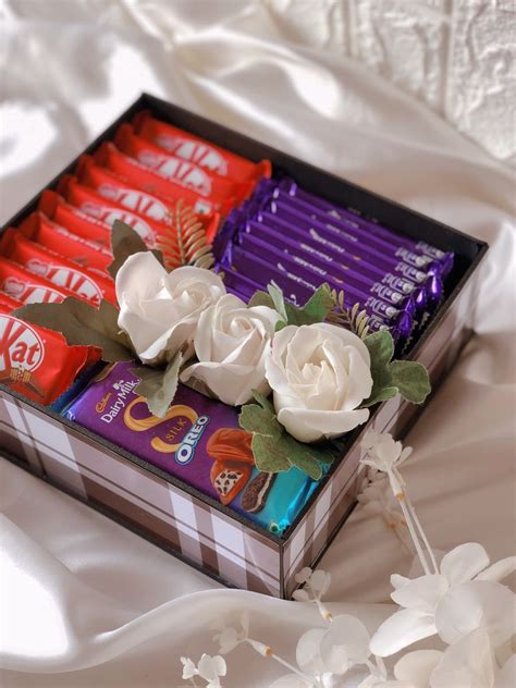 An Assortment Of Chocolates In A Box With Flowers On The Side And White