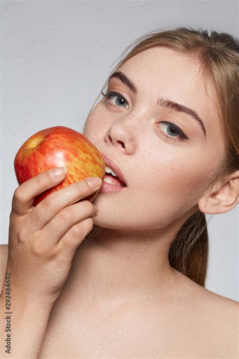 Close Up Portrait Of A Blond Girl With Naked Shoulders She Bites A Red Apple Girl Has Nude
