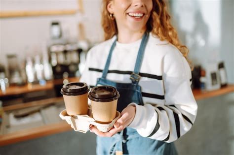 Premium Photo A Barista Woman In An Apron Holds Hot Coffee In A Paper