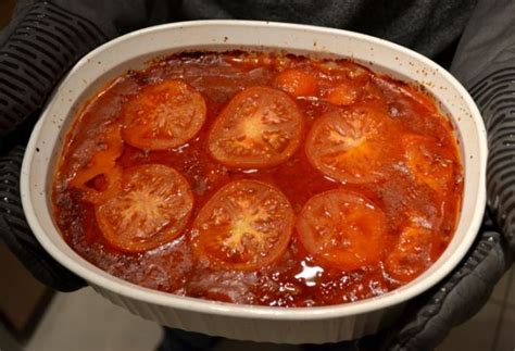 A Person Holding A White Bowl Filled With Cooked Tomatoes And Sauce On