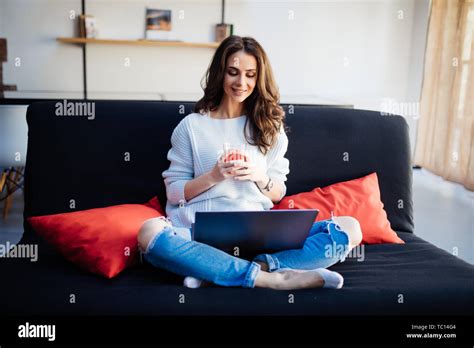 Smiling Beautiful Brunette Relaxing On The Couch And Using Her Laptop In The Living Room Stock