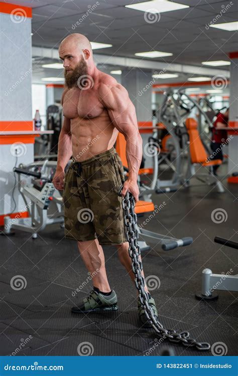 A Bald Bearded Bodybuilder With Large Relief Muscles Holds A Heavy