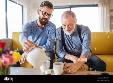 An Adult Hipster Son And Senior Father Sitting On Sofa Indoors At Home