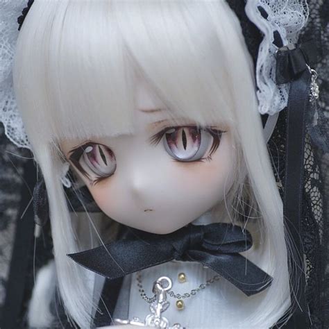 A Close Up Of A Doll With Blonde Hair And Big Eyes Wearing A White Dress