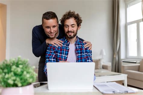 Encantadora pareja gay riendo juntos mientras están sentados en su sala