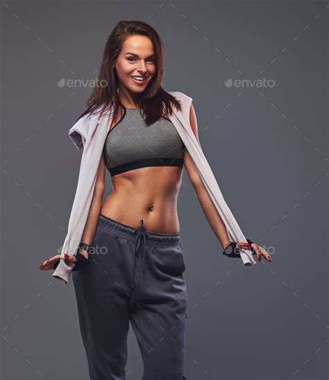 Smiling Fitness Brunette Woman In A Gray Sportswear Posing In A Studio