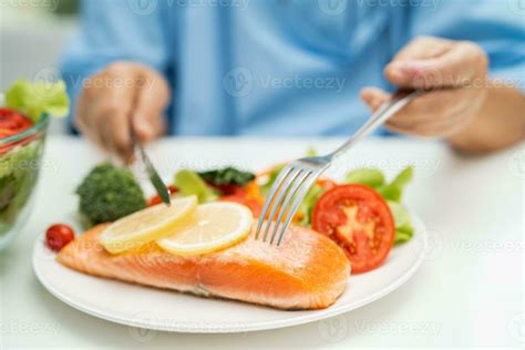 Asian elderly woman patient eating salmon steak breakfast with