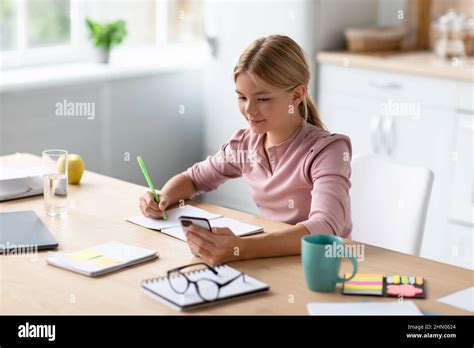 Cheerful European Blonde Teen Girl Pupil Learning Remote By Phone Using App Watching Online