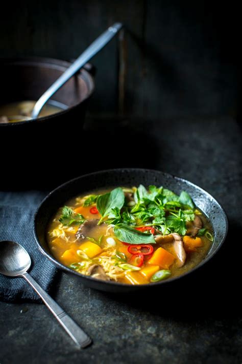 A Bowl Filled With Soup Next To A Spoon On Top Of A Black Tablecloth