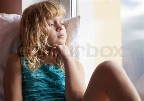 Little blonde verschlafenen Mädchen Sitz mit Kissen auf der Fensterbank in hellen Morgenlicht