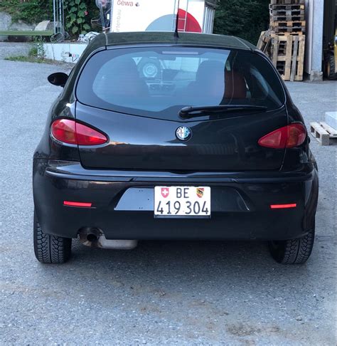 The Back End Of A Black Car Parked In Front Of A Building With A Sign On It