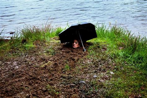 A Woman Is Hiding Under An Umbrella In The Mud By The Water S Edge