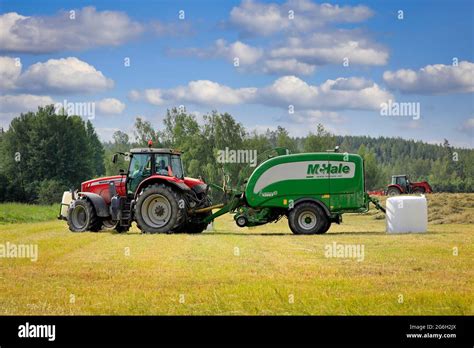 Massey Ferguson Tractor In Hay Field With Mchale Baler Wrapper Harvesting Dry Hay In The Summer