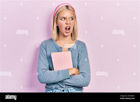 Belle femme blonde tenant le livre en colère et fou hurlant frustré et furieux criant avec