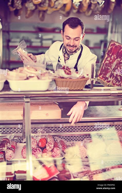 Male Shop Assistant Demonstrating Assortment Of Sausages In Butchers