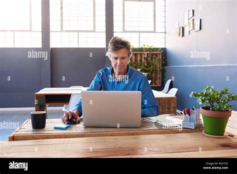 Smiling Mature Businessman Sitting Alone At His Desk In A Large Modern