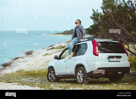 Man Sitting On The Car Roof Enjoying View Of Summer Sea Vacation