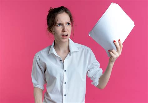 Jeune fille russe blonde agacée détient des feuilles de papier à côté isolé sur espace rose avec