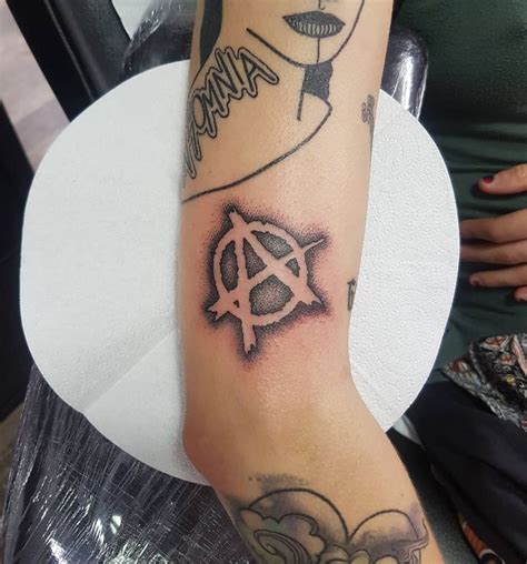 A Woman S Arm With Tattoos On It And An Anarchy Symbol In The Middle