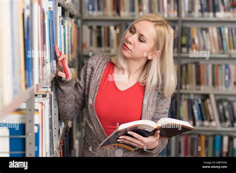 Pretty Woman With Blonde Hair Standing In The Library Blurred Books At The Back Stock Photo