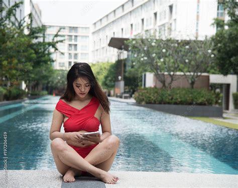 The Lady In Bikini Suit Is Sitting Beside Swimming Pool She Is Holding Taplet In Hand Blurry