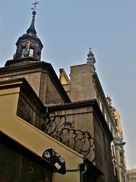 An Old Building With Graffiti On It S Side And A Steeple In The Background