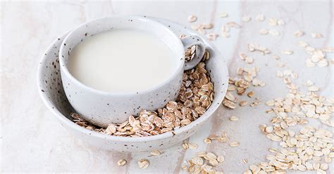 A cup of oat milk in bowl of oats on a marble surface - ProHealth