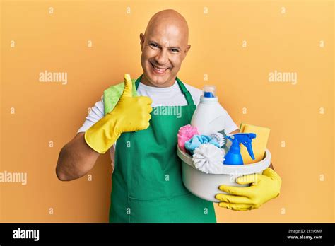 Middle Age Bald Man Wearing Cleaner Apron Holding Cleaning Products