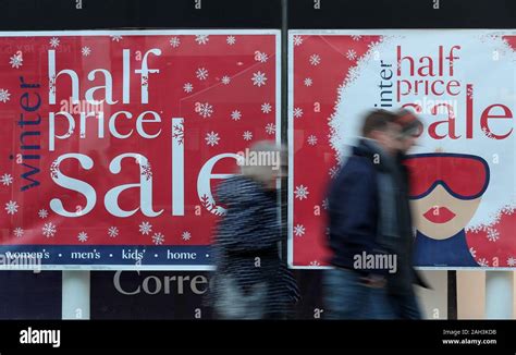 Christmas Shoppers Walk Past A Sale Sign In The Window Of Debenhams On