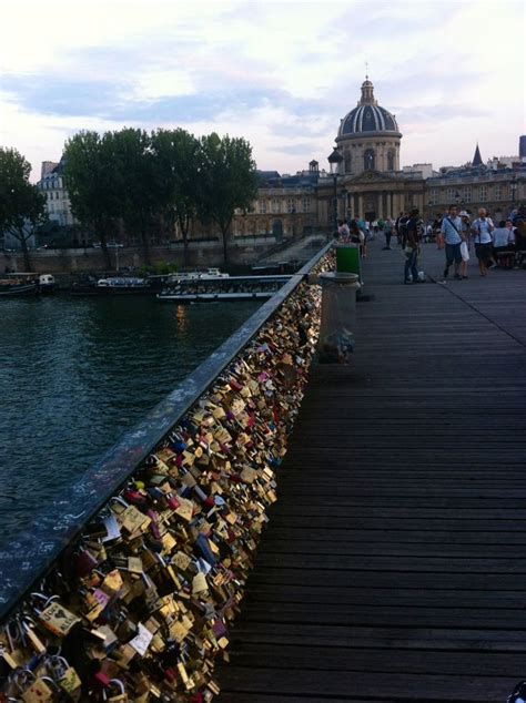 Many Padlocks Are Attached To The Bridge By The Water And People Walk