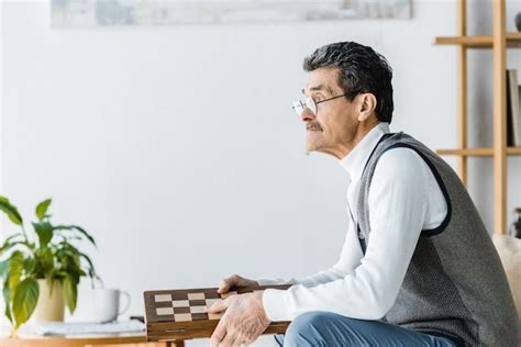 Pensionista Pensativo Con Gafas Sosteniendo Un Tablero De Ajedrez En