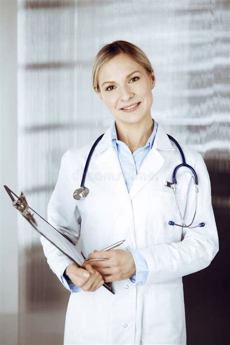 Friendly Female Doctor Standing In Sunny Clinic Portrait Of Cheerful