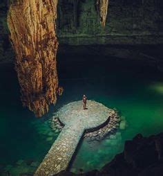 A Person Standing On The Edge Of A Body Of Water In Front Of A Cave