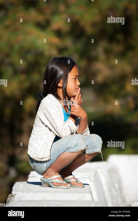 Young Bhutanese girl wearing Western clothing squatting in sun near ...