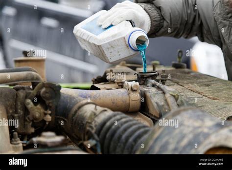 An Auto Mechanic Pours Antifreeze Into The Radiator Of An Old Car