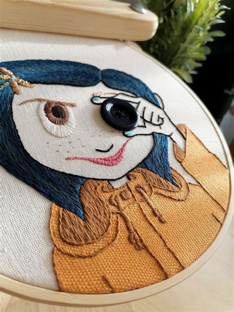 A Close Up Of A Embroidery On A Wooden Table With A Plant In The Background