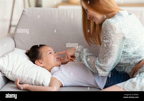 Happy Mother Touching Daughters Nose Laughing Sitting On Sofa Indoor