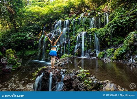 Excited Caucasian Woman Raising Arms In Front Of Waterfall View From