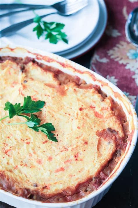 Lentil Vegetarian Cottage Pie In A White Baking Dish Stack Of Plates