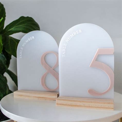 Two White And Pink Table Numbers Sitting On Top Of A Wooden Stand Next