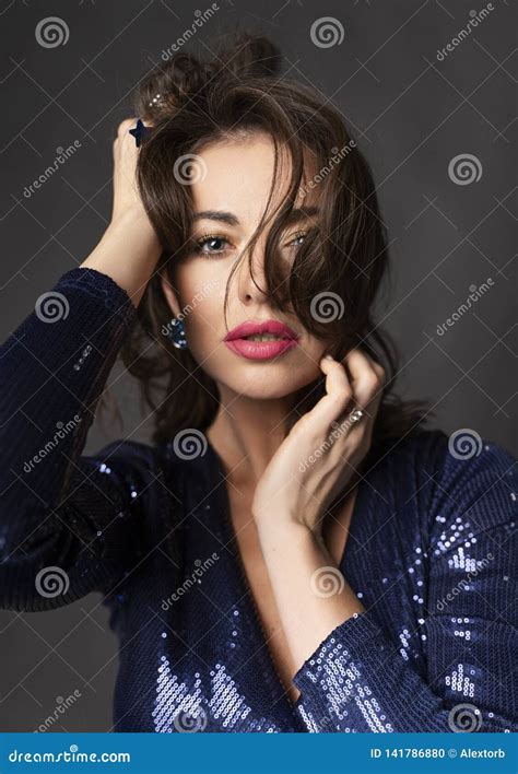 A Beautiful Brunette Woman Wearing A Glittery Blue Dress Against A Gray