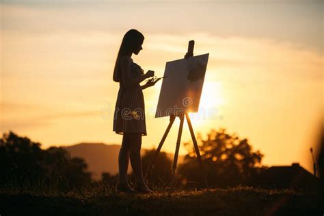 La Silueta De Una Muchacha Del Blonde Pinta Una Pintura En La Lona Con La Ayuda De Las Pinturas