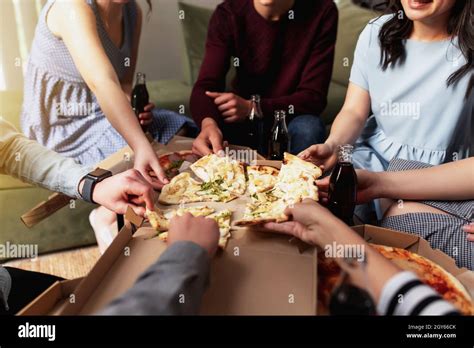 A pizza party, a group of friends chatting and happily eating pizza at the table and drinking ...