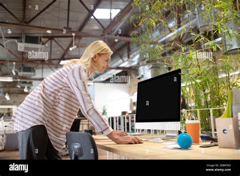 Blonde Woman Bending Over Desk Looking At Screen Stock Photo Alamy
