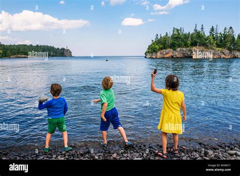 Three children throwing rocks into a lake Stock Photo - Alamy