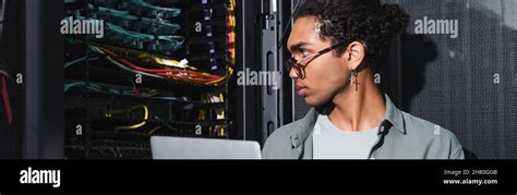 African American Engineer With Laptop Looking At Wires In Server While